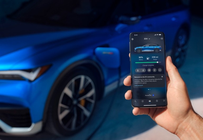 2024 Acura ZDX Type S in Apex Blue Pearl charging on background, on foreground a phone with the interface of Acura EV app